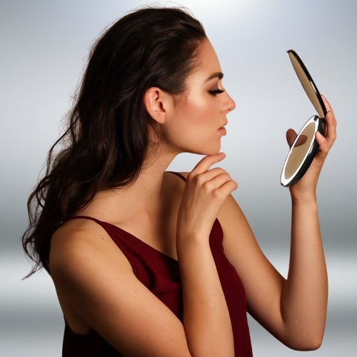 Femme utilisant un miroir de poche LED pour une retouche maquillage précise