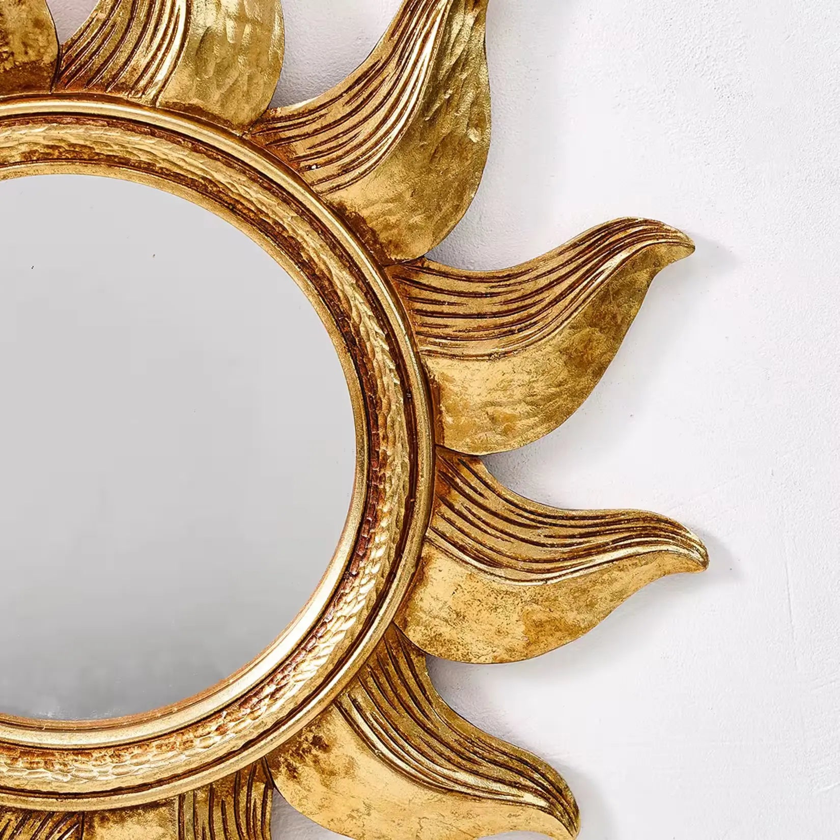 Gros plan sur les rayons sculptés et la patine dorée du miroir décoratif baroque.