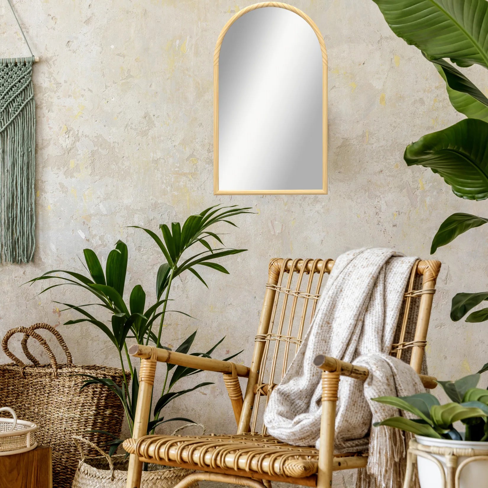 Coin cosy avec fauteuil en rotin, plaid texturé et miroir arche bois sur mur beige.
