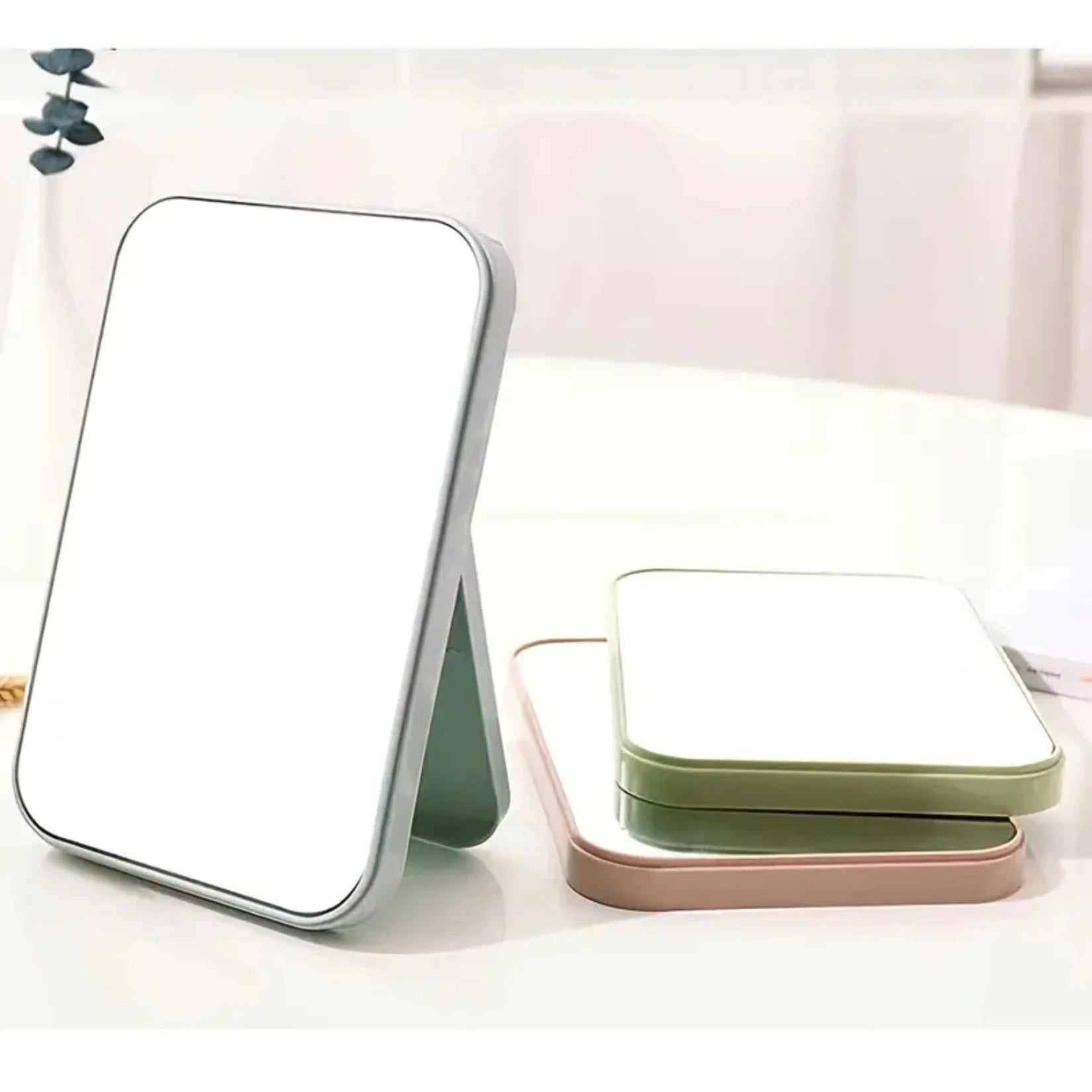 Miroir de poche rectangulaire gris debout à côté de modèles vert et rose empilés.