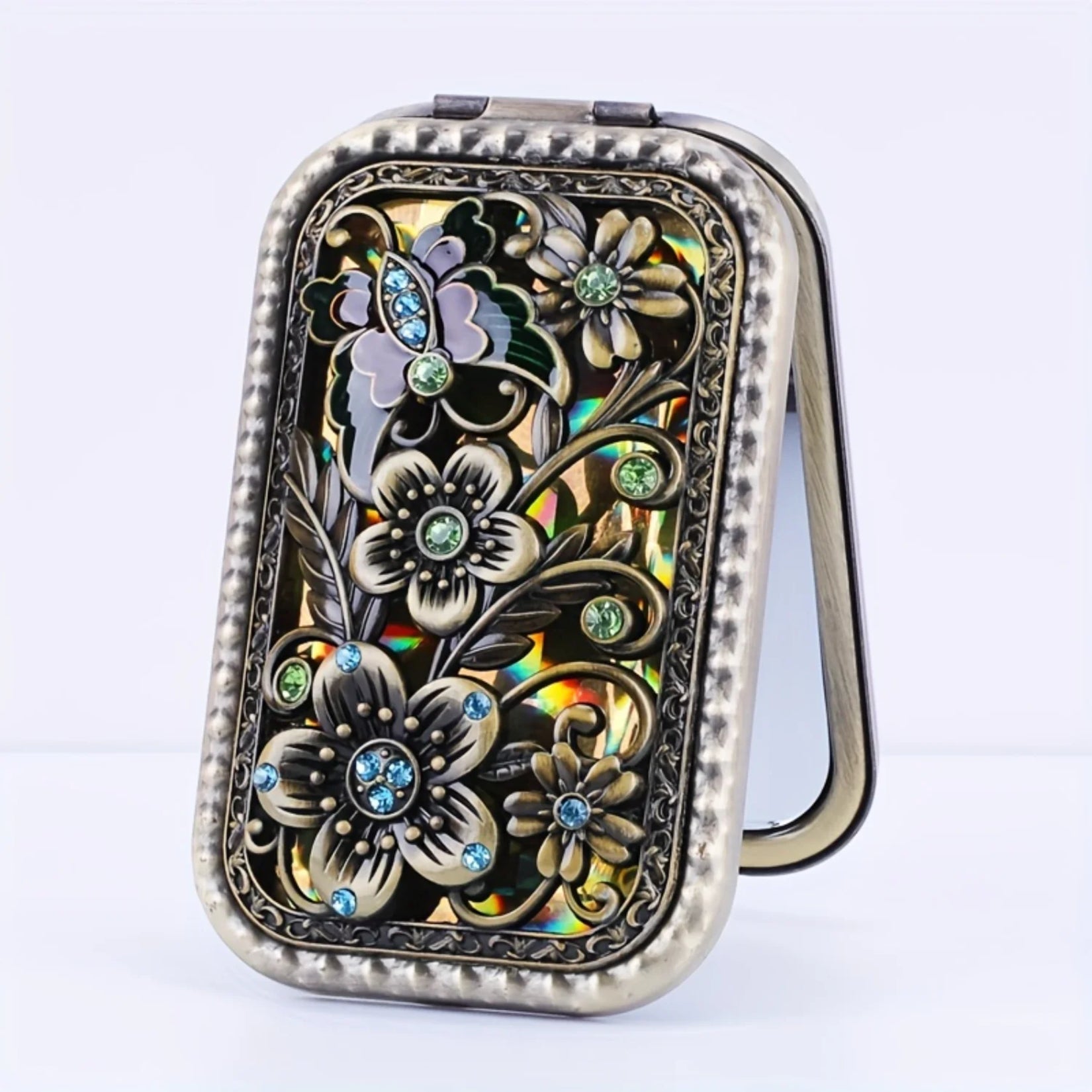 Face avant du miroir de poche vintage avec motifs floraux incrustés de pierres colorées.