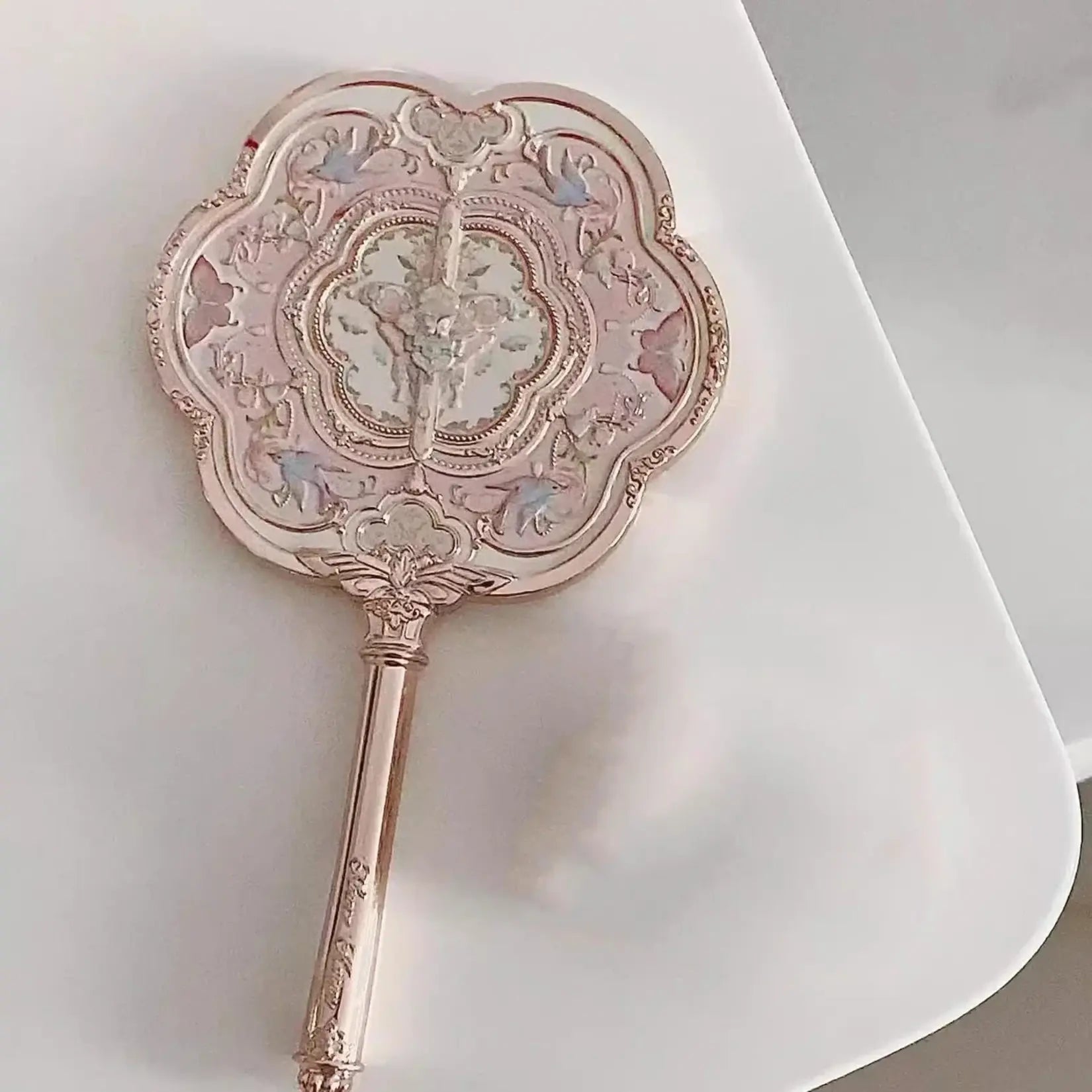 Miroir de poche vintage rose pâle en métal avec manche décoratif style baroque.