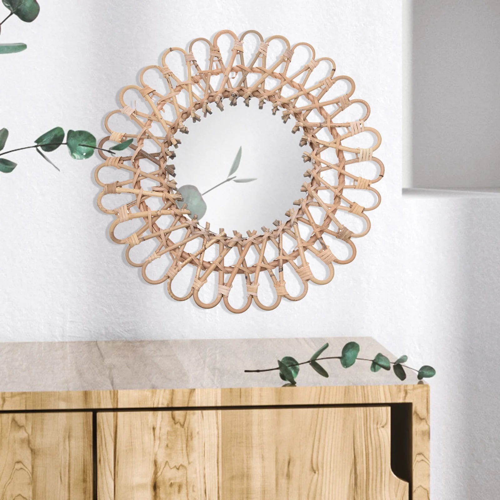 Miroir fleur rotin fixé sur mur blanc au-dessus d’un meuble en bois clair, décor naturel.