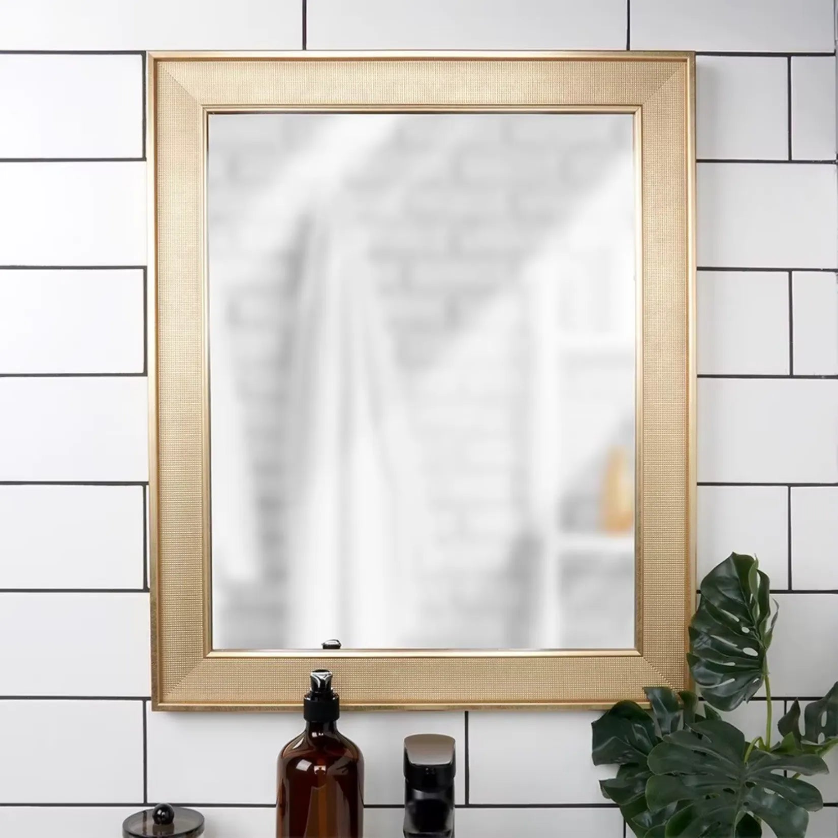 Miroir mural doré à cadre rectangle installé dans une salle de bain au carrelage blanc.