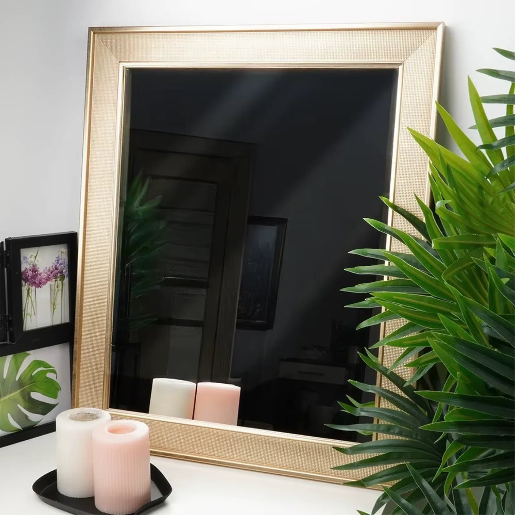Miroir mural doré posé sur meuble blanc avec plantes et bougies décoratives.