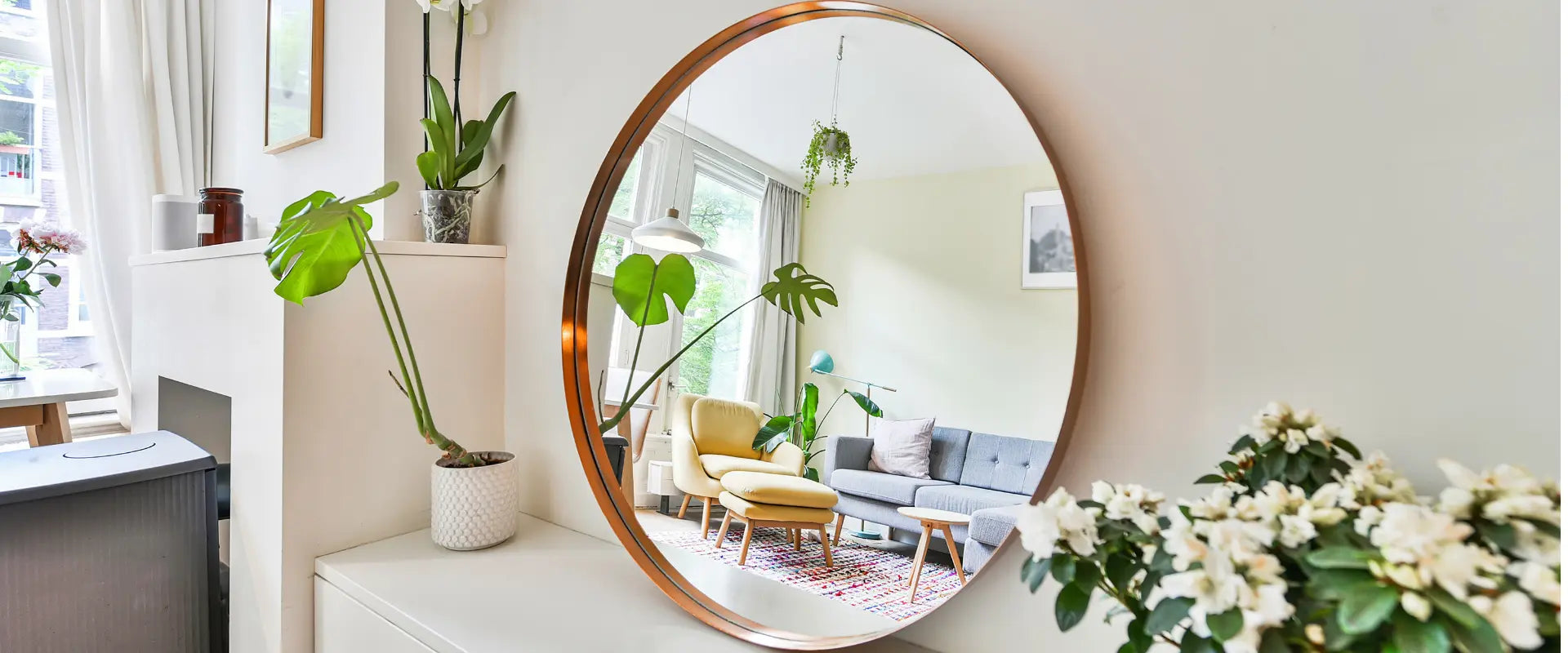 Grand miroir rond avec cadre cuivré reflétant un salon lumineux avec plantes vertes.