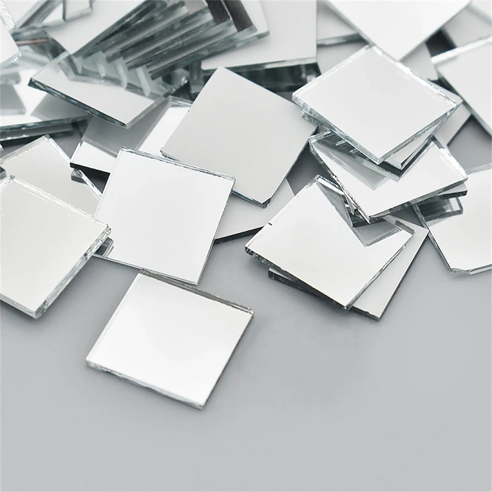 Carreaux mosaïque miroir verre argent 10x10 mm empilés, vue rapprochée fond gris.