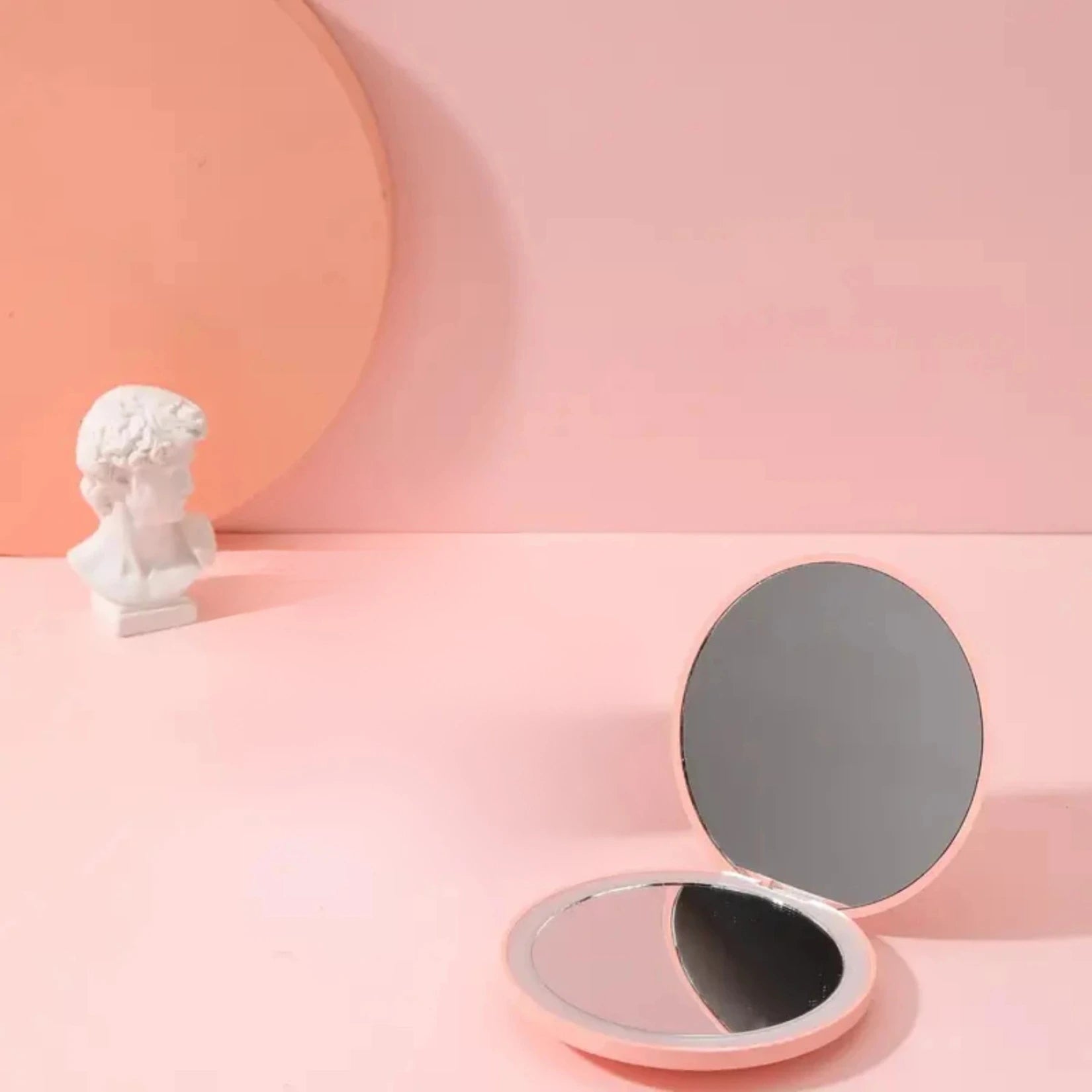 Petit miroir de poche posé sur une table dans un décor rose.