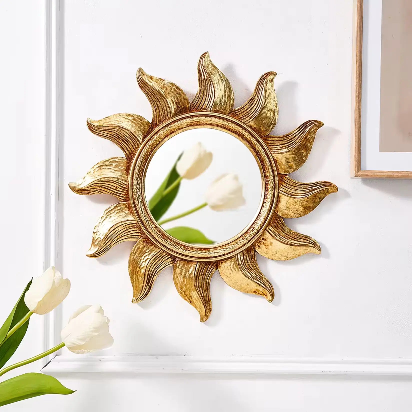 Petit miroir doré rond design soleil accroché sur mur blanc avec décoration florale.