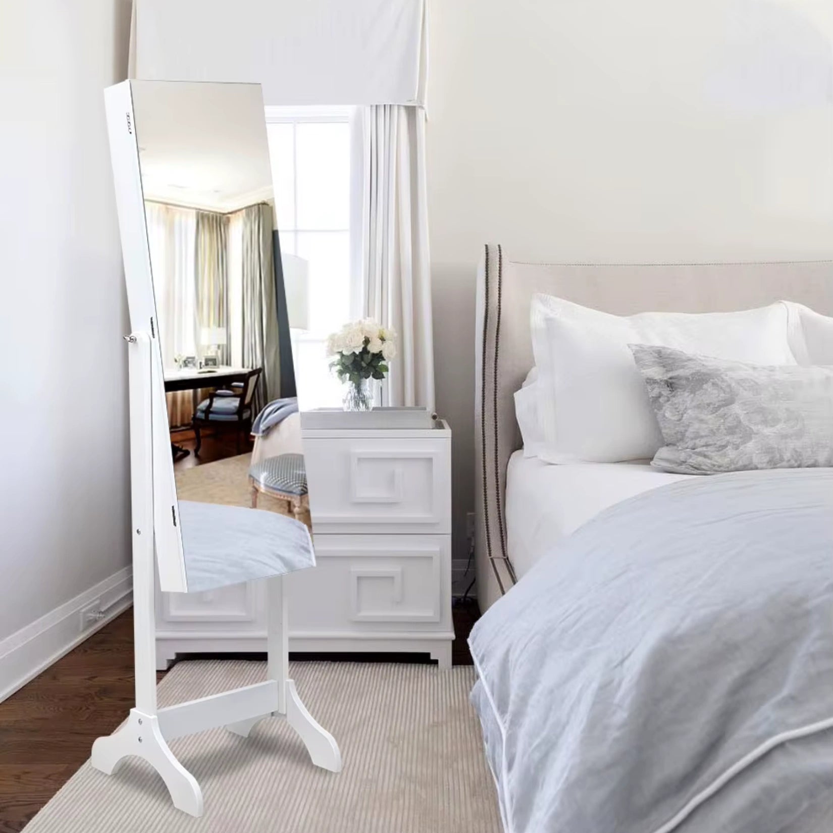 Armoire à bijoux miroir sur pied installée dans une chambre à la décoration blanche.