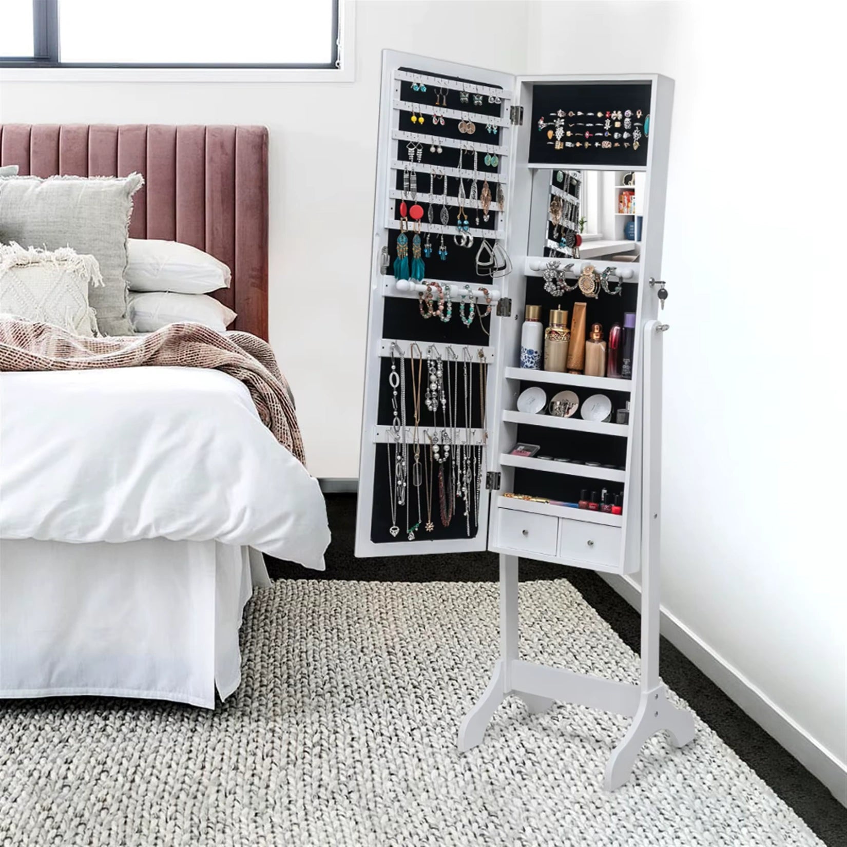 Armoire à bijoux miroir sur pied installée dans une chambre avec lit et tapis moderne.