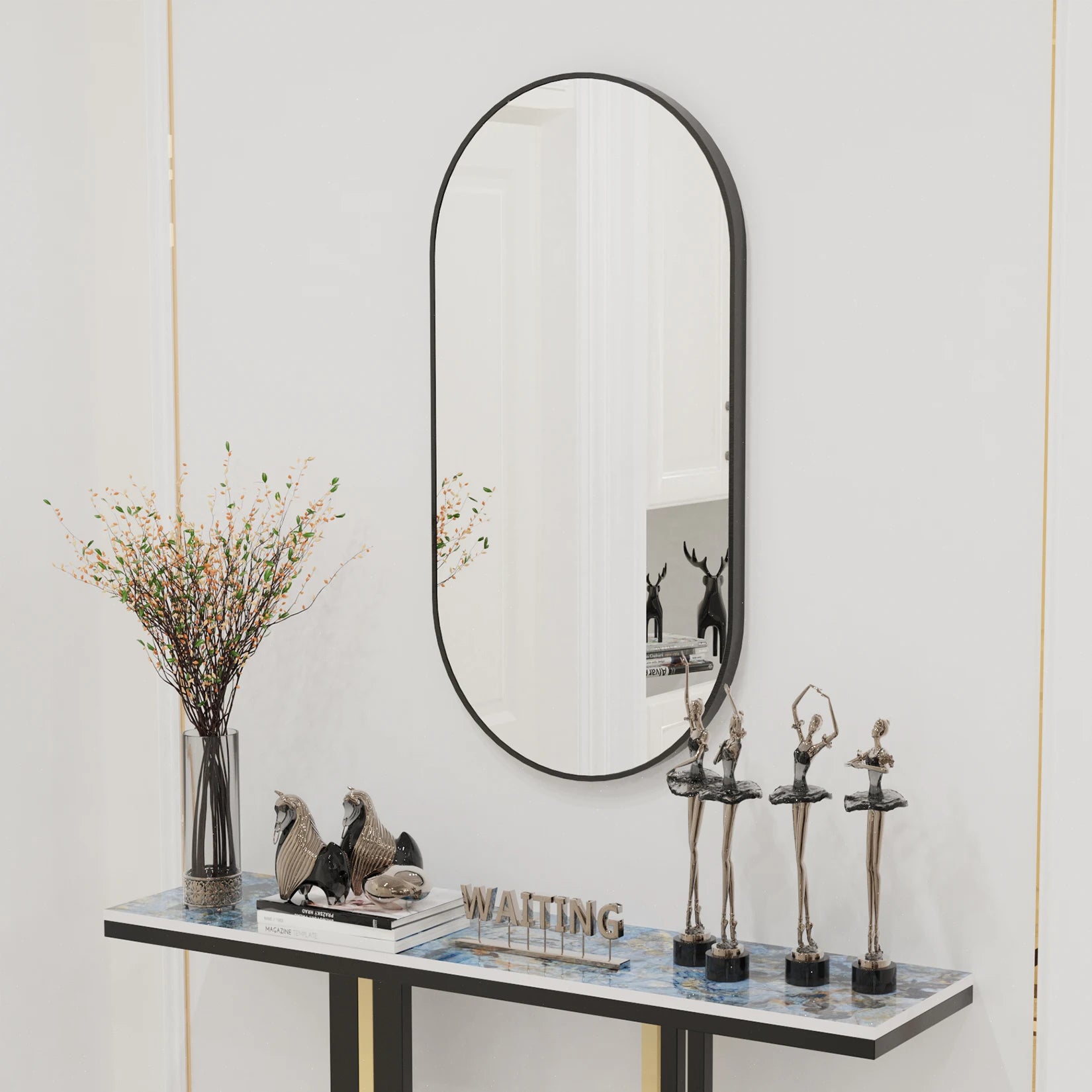 Grand miroir mural ovale noir suspendu dans une entrée raffinée avec objets décoratifs.