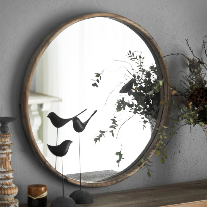 Grand miroir rond bois avec décor végétal en arrière-plan.