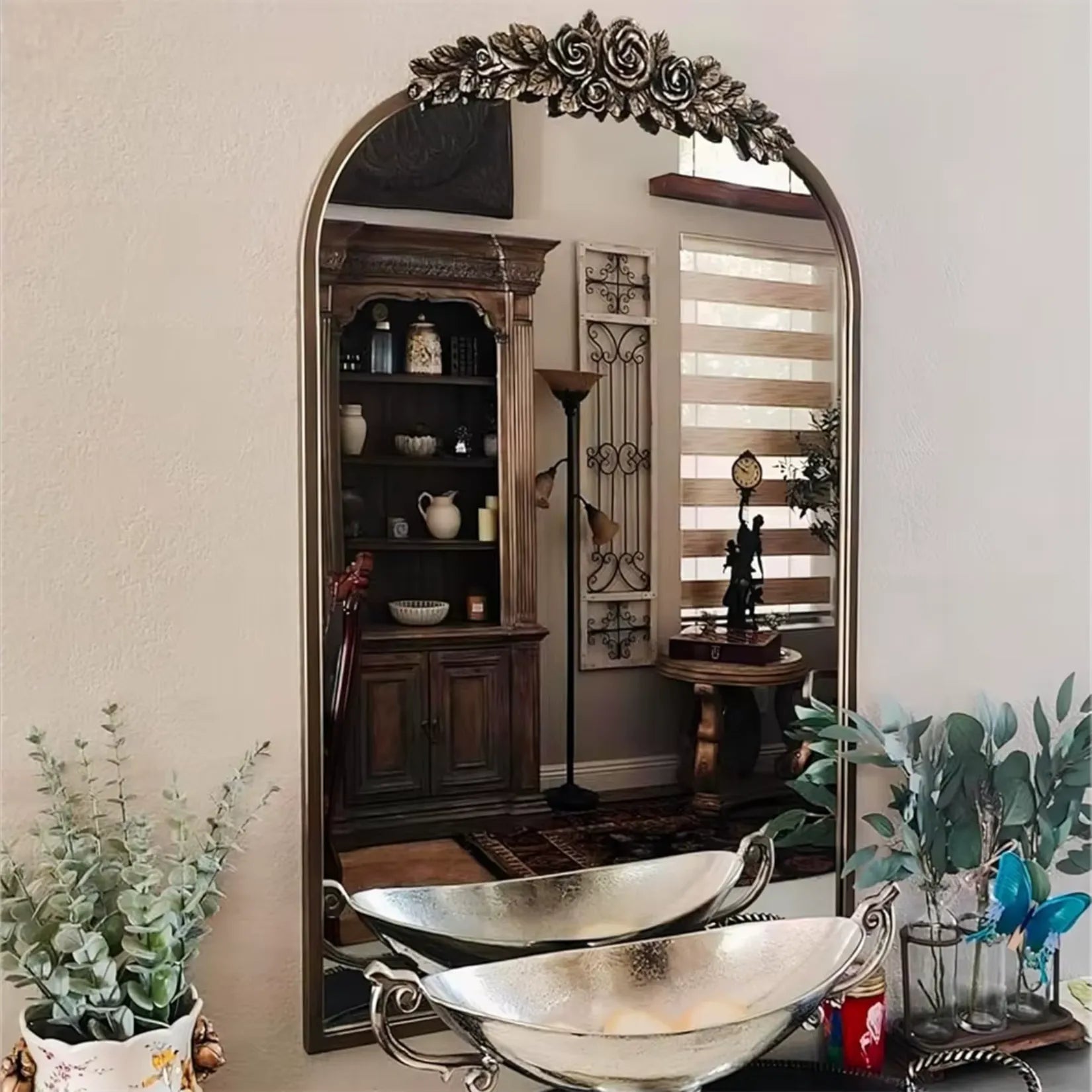 Miroir baroque doré placé dans une salle de bain au style ancien, avec vasques en métal argenté et déco végétale rustique.