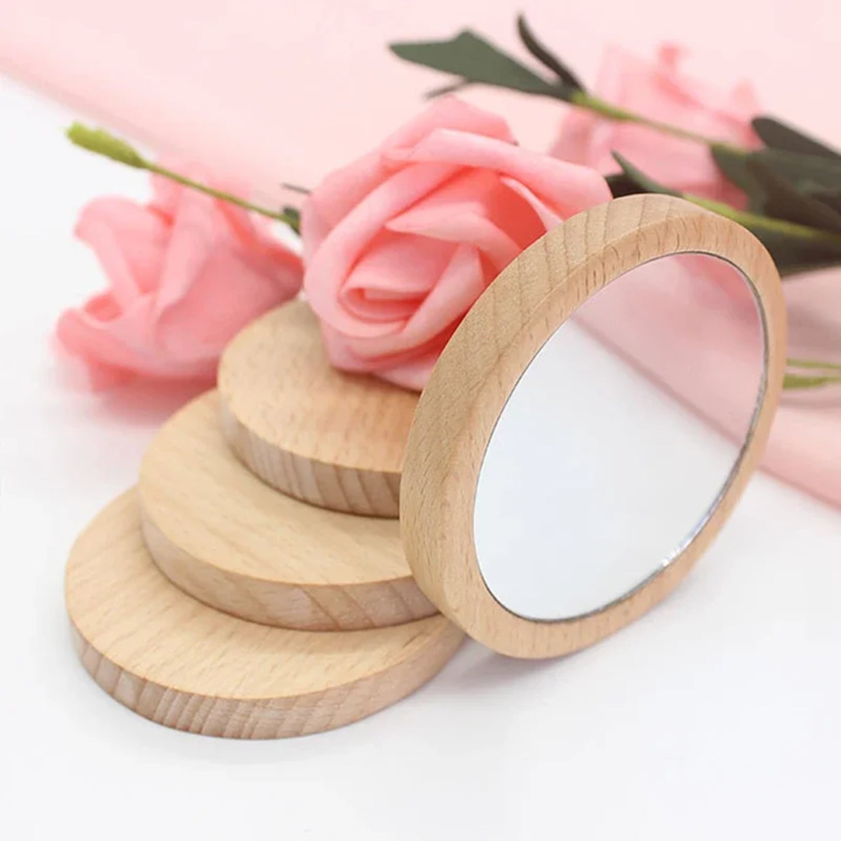 Miroir de poche bois posé sur un tissu avec des roses roses en arrière-plan.