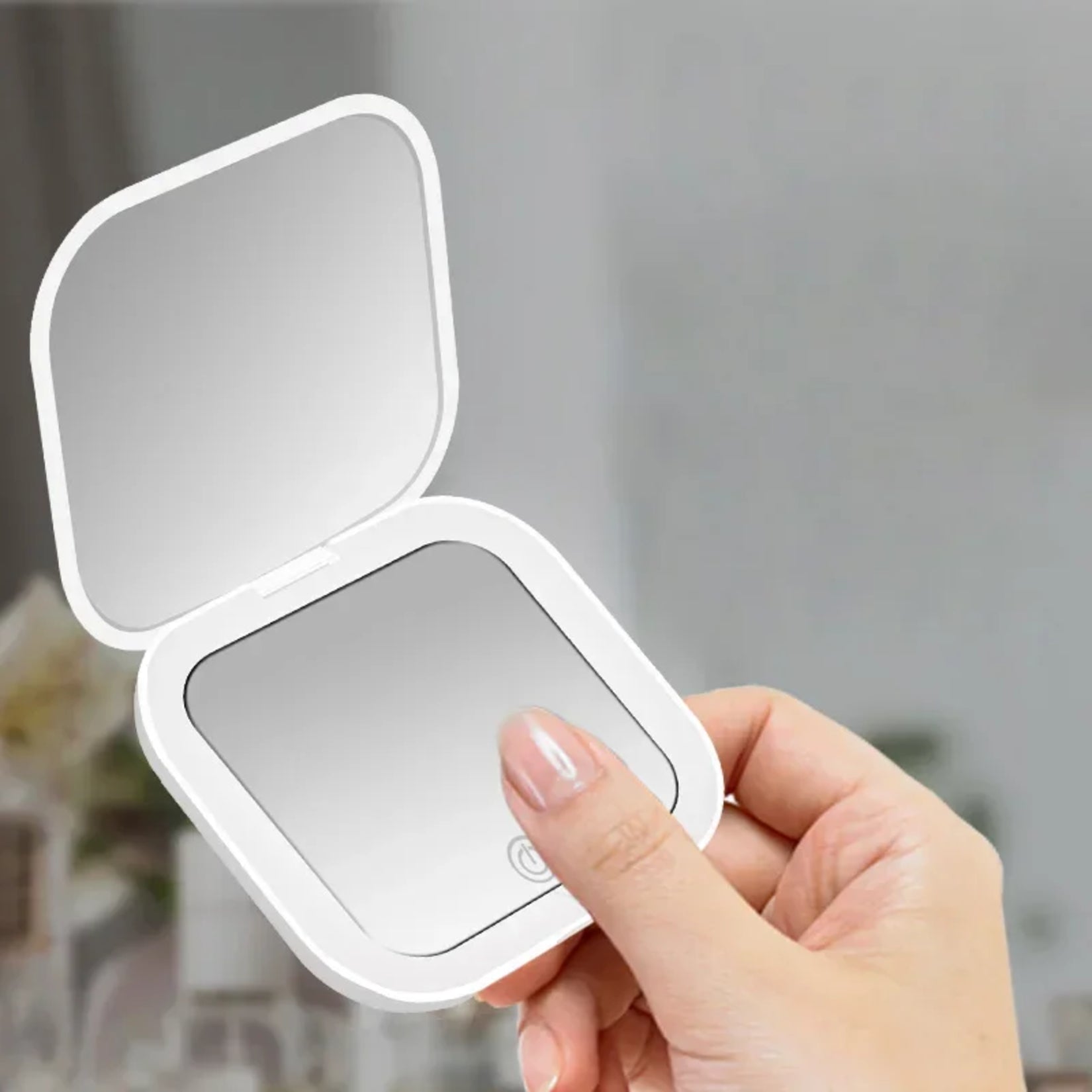 Miroir de poche grossissant blanc tenu en main pour une utilisation facile.