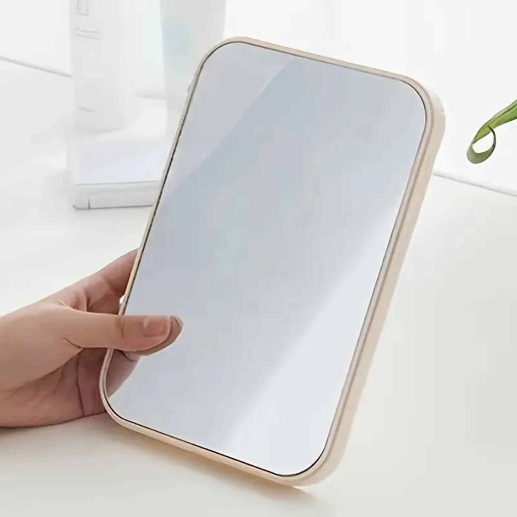 Miroir de poche rectangulaire crème anglaise tenu à la main sur une coiffeuse blanche.