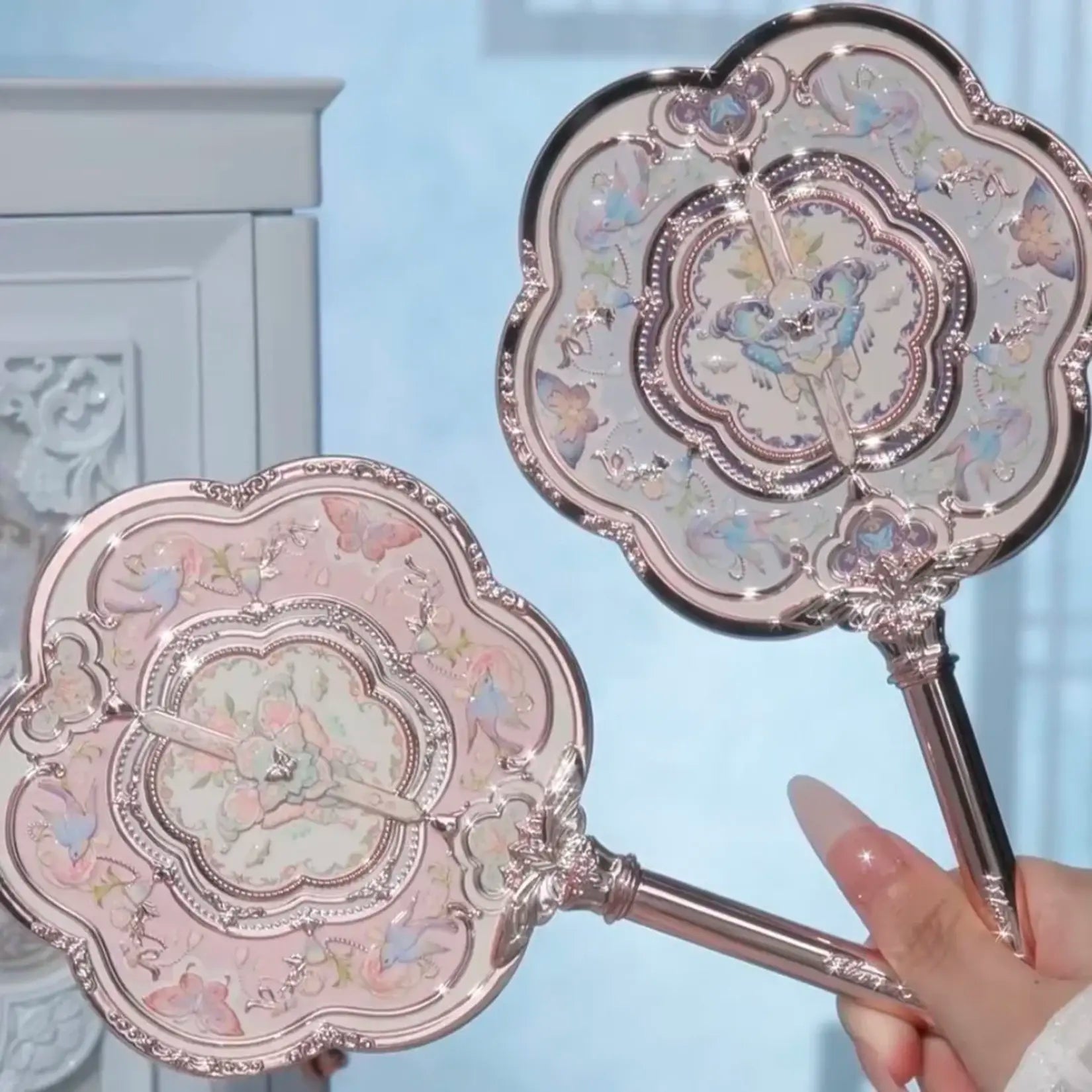 Miroir de poche vintage rose en métal avec manche sculpté et motifs floraux baroques.