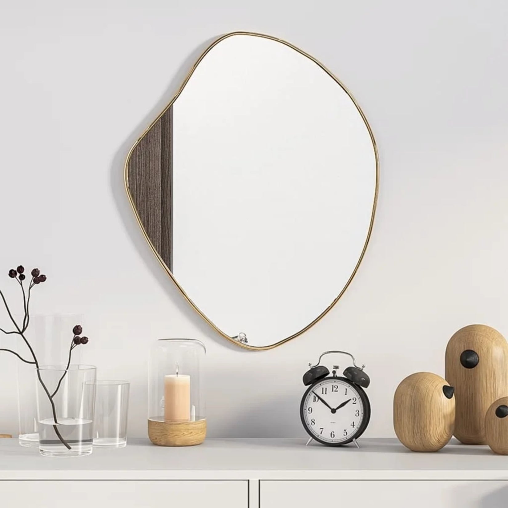Miroir irrégulier doré au-dessus d’une console décorée d’objets et d’une bougie.
