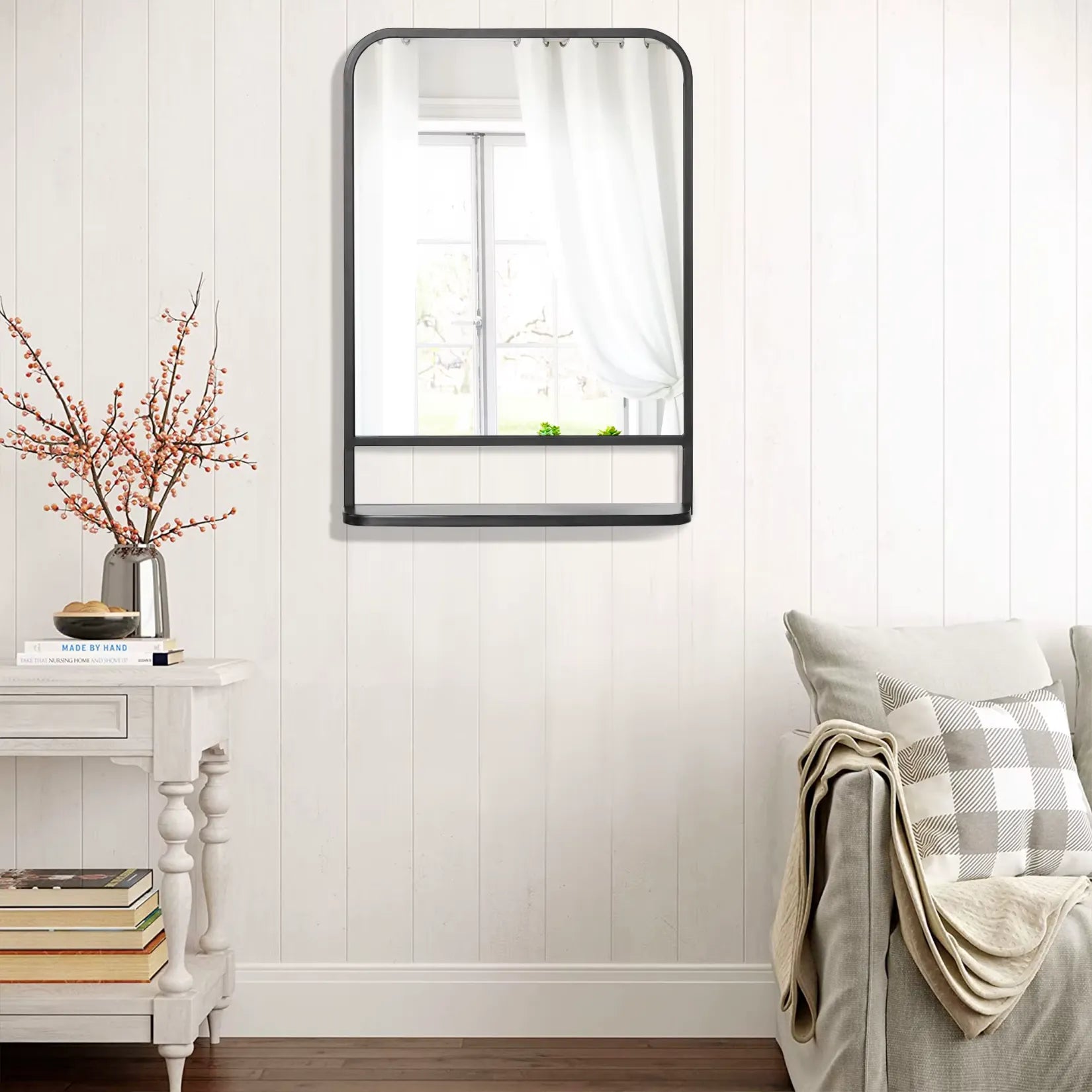 Miroir métal industriel avec étagère contre un mur blanc avec fauteuil beige.