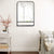 Miroir métal industriel avec étagère contre un mur blanc avec fauteuil beige.