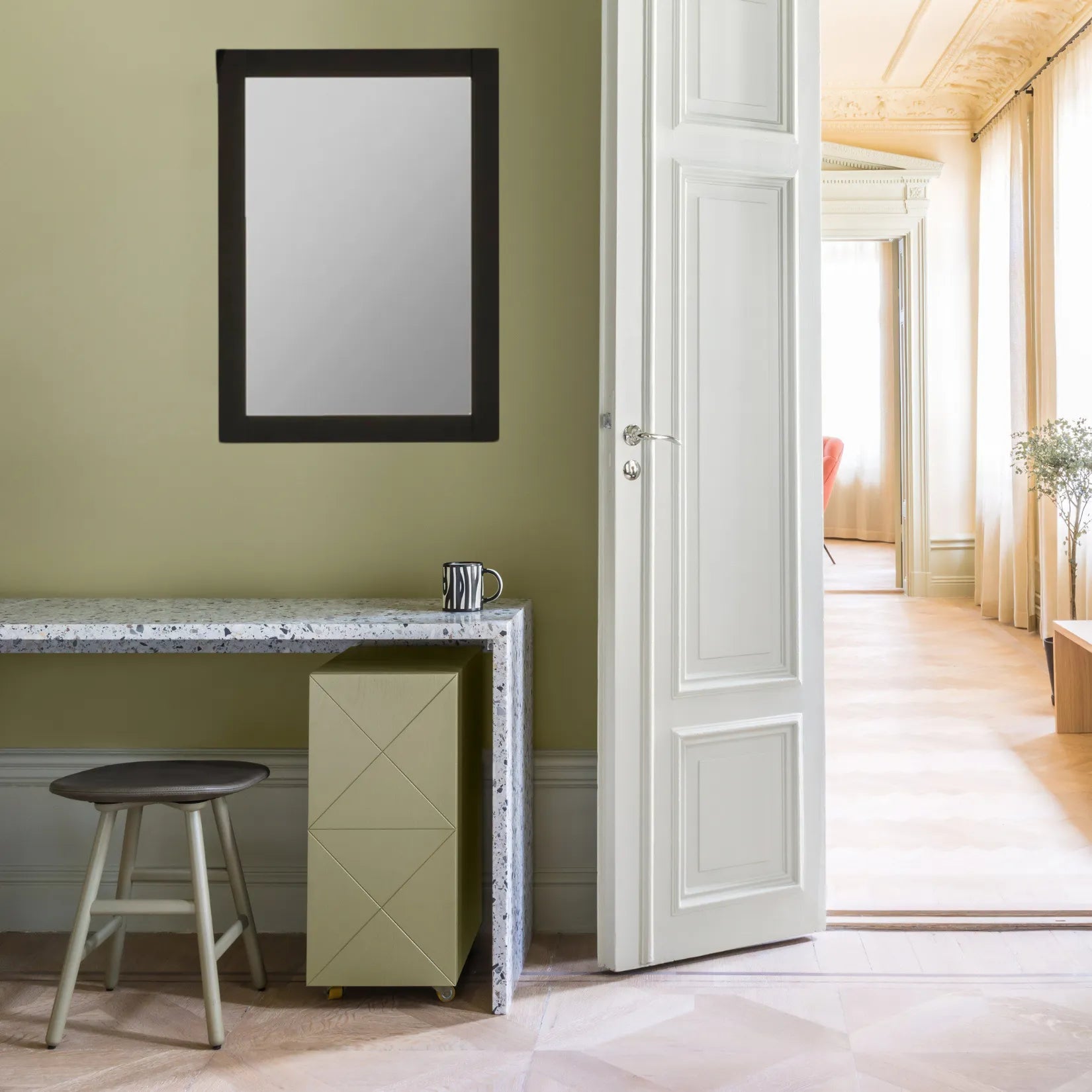 Miroir minimaliste noir accroché sur un mur vert dans une pièce au style classique revisité.