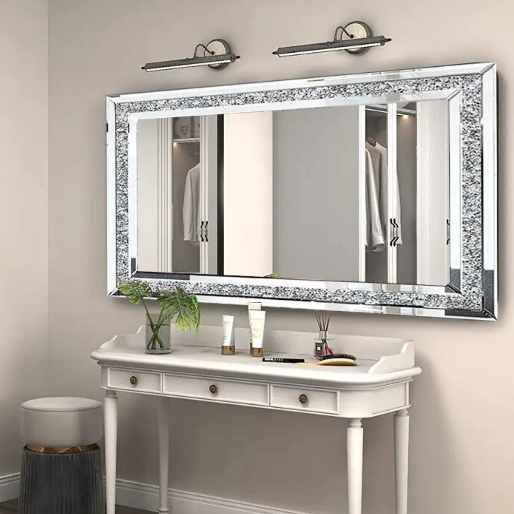 Miroir mural rectangulaire design avec cristaux incrustés installé au-dessus d’une coiffeuse blanche.