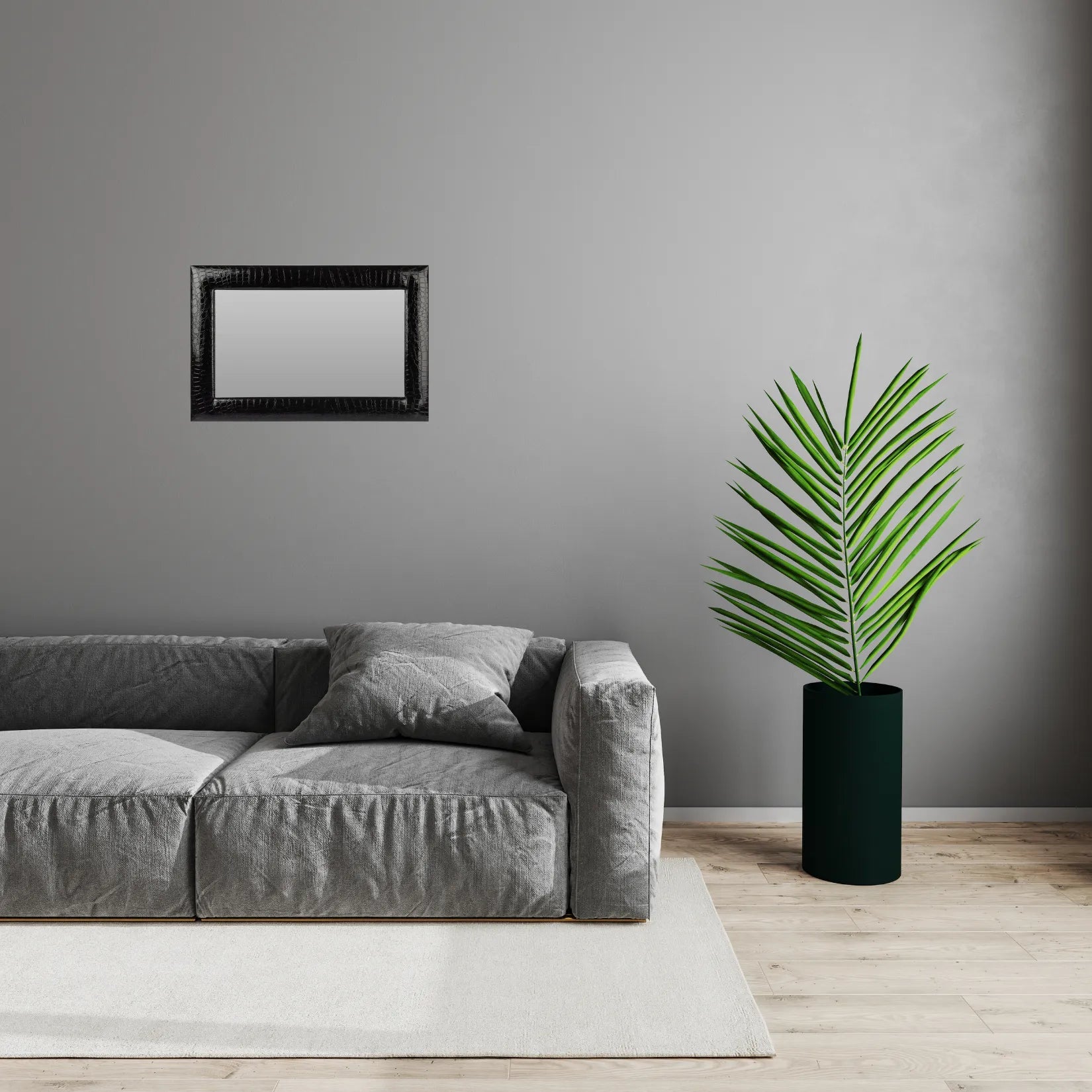 Miroir noir rectangulaire accroché sur un mur anthracite, au-dessus d’un canapé gris.