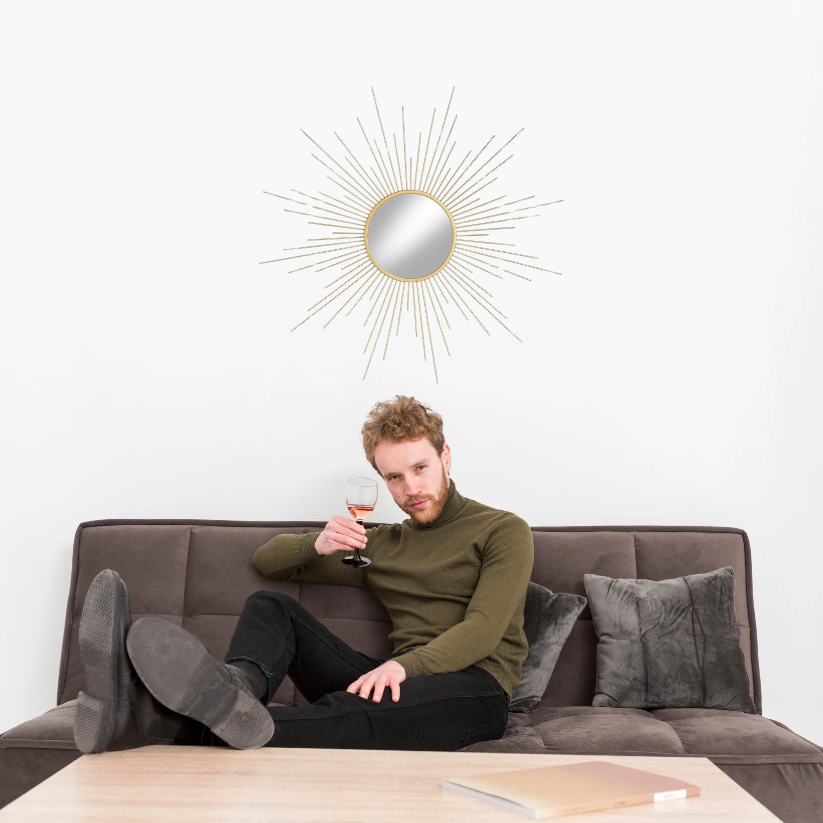 Miroir soleil doré suspendu au mur au-dessus d’un canapé – style rétro chic.