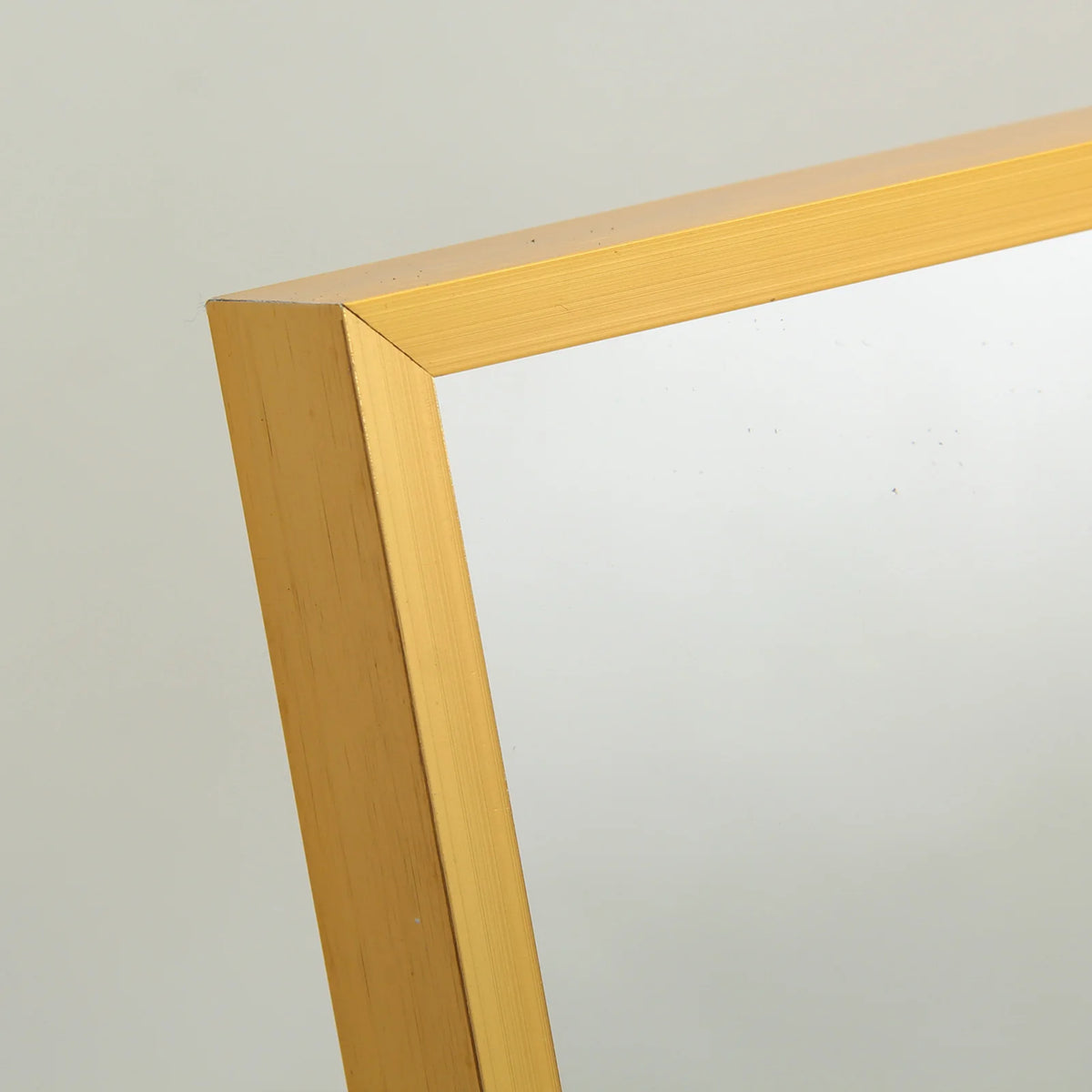 Détail du cadre en métal doré satiné du miroir sur pied doré avec finition soignée.