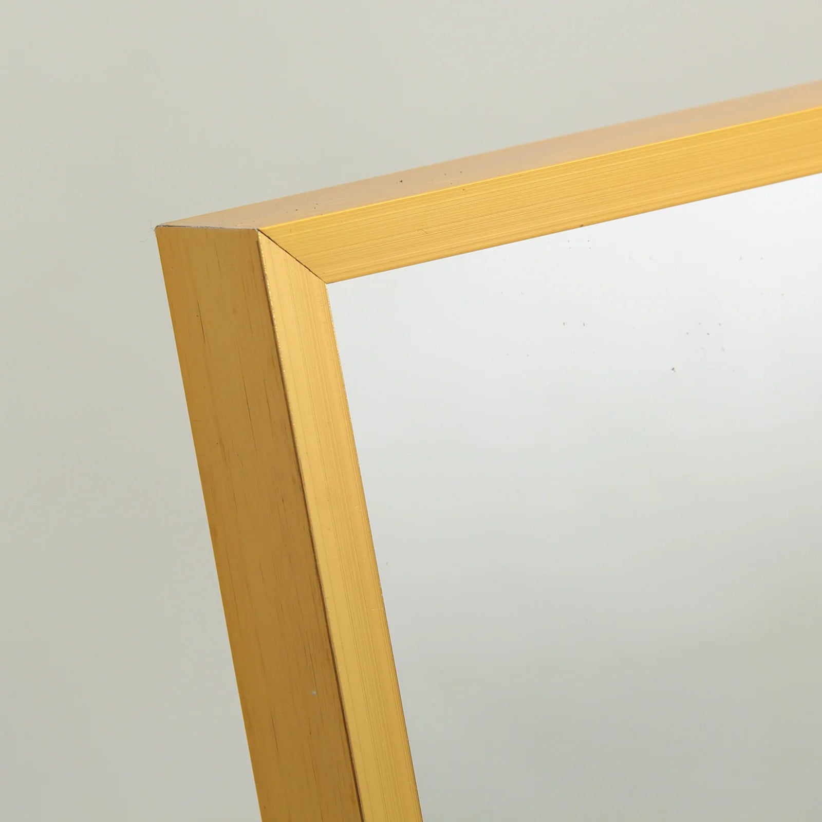 Détail du cadre en métal doré satiné du miroir sur pied doré avec finition soignée.