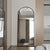Miroir sur pied noir XXL avec arc arrondi dans un intérieur épuré et lumineux.