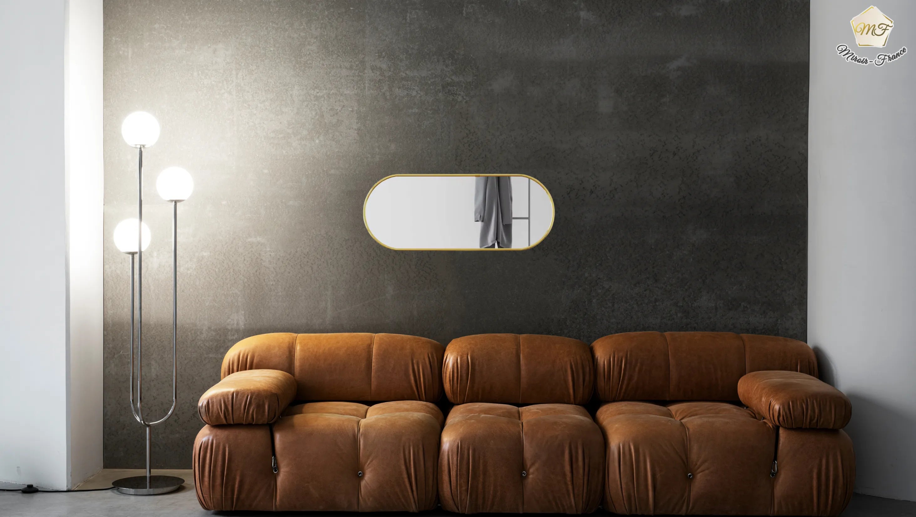 Petit miroir doré mural installé dans un salon avec canapé cuir vintage.